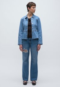 Lichtblauw spijkerjasje met knoopsluitingen en een elastische taille, gecombineerd met lichtblauwe jeans met rechte pijpen en een scheur bij de knie.