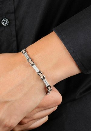 Bracciale in metallo argentato con un design a rete composto da elementi rettangolari e finiture lucide. Indossato su un polso contro un tessuto scuro.