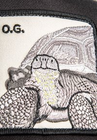 Embroidered patch featuring a tortoise design in shades of gray and tan, with textured detailing and black border, on a light background.