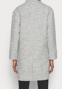 Szary płaszcz o jodełkowym wzorze z wysokim kołnierzem, długimi rękawami i prostym krojem. Strukturalna tkanina z subtelnymi, kontrastującymi nitkami.