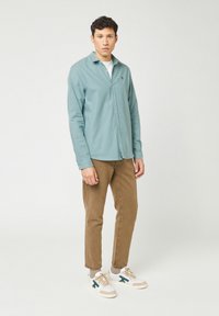 Lichtgroene geblokte overhemden van katoen, gecombineerd met tan broek en witte sneakers met groene accenten.
