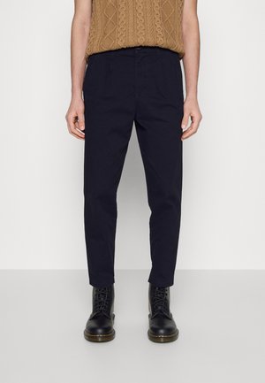 Pantalon bleu marine en mélange de coton, avec une coupe fuselée, passants de ceinture et poches latérales. Associé à des bottes noires à lacets.