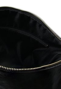 Intérieur d'un sac en cuir noir avec une texture lisse, fermeture éclair en métal doré, avec une petite poche sur un côté.