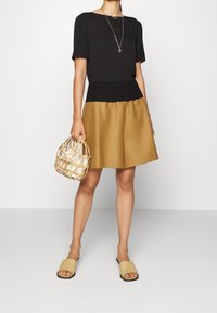 Top negro, falda A-line dorada y sandalias beige. Los accesorios incluyen un bolso de mimbre. La ropa se caracteriza por su tela suave y un corte relajado.