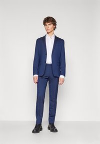 Navy blue suit with a tailored fit, single-breasted jacket, and notch lapels. Accompanied by a white dress shirt and black shoes.