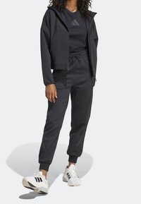 Svart träningsset med en zip-up jacka med stora fickor och matchande joggers. Vita sneakers med svarta detaljer fulländar looken.