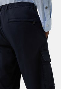 Marine cargo bukser med elastisk talje, sidelommer og en baglommem med lynlås. Stoffet er glat med en subtil glans.