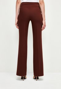 Hnědé kalhoty s širokým střihem a hladkým povrchem, středně vysokým pasem a švy, doplněné o černé lodičky na podpatku.