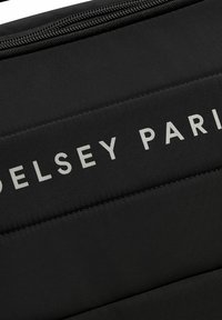 Bolsa de tela negra con costuras verticales y un logo en relieve gris "Delsey Paris". Presenta un cierre de cremallera. Textura suave y duradera.