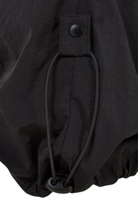 Zwarte stoffen trekkkoord met een plastic schuifregelaar en een drukknoop, met een textuuraanraking en een geplooide onderkant voor verstelbare sluiting.