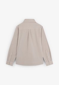 Camisa de manga larga color beige claro con cuello, detalle de plisado en la espalda y puños con botón. Textura suave y diseño entallado.