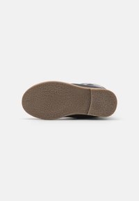 Chaussure noire avec une semelle en caoutchouc texturée ; présente un design plat et un petit talon ; inclut une indication de taille visible sur la semelle.