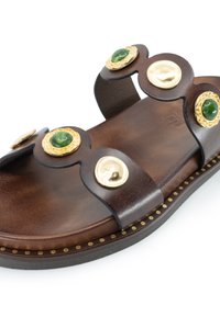 Sandalo in pelle marrone con cinturini curvi, hardware dorato, pietre verdi e cuciture decorative lungo la suola.