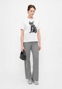 White t-shirt with a black graphic of a dog, paired with black-and-white striped wide-leg pants, and silver sneakers. Black handbag with eyelets.