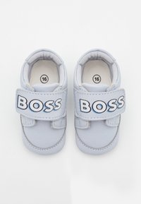 Ljusblå barnskor i storlek 16 med en slät, syntetisk yta, utrustade med kardborreband och djärv "BOSS"-logotyp på sidan.