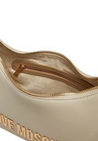 Borsa con zip color crema e hardware dorato, dotata di una tasca interna e texture liscia. Logo "LOVE MOSCHINO" impresso sulla parte anteriore.