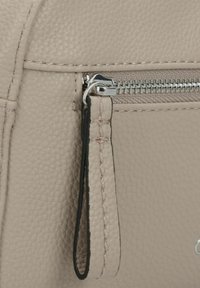 Bolso de mano texturizado beige por un lado con un cierre metálico, que cuenta con un tirador de cremallera y costuras en hilo negro que contrastan a lo largo de la costura.