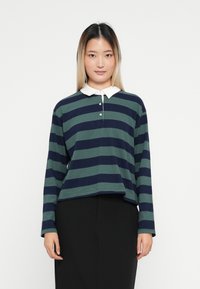 Langermige polo shirt in donkergrijze en marineblauwe strepen, met een witte kraag en drie knopen. Ontspannen pasvorm en zachte katoenen textuur.