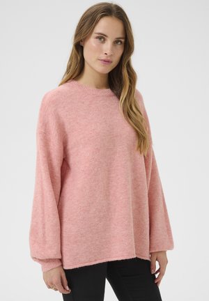 Light pink, loose-fitting sweater with a crew neck and long sleeves. Soft texture and ribbed cuffs. Paired with dark pants.