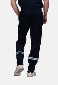Marineblauwe joggingsbroek met lichtblauwe horizontale strepen bij de boorden; elastische tailleband; zacht materiaal; ritsboorden voor een verstelbare pasvorm.
