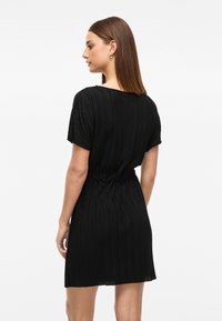Vestido preto plissado com um corte descontraído, mangas curtas e um cinto elástico. O tecido possui um acabamento texturizado, realçando o design.