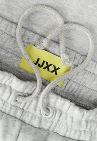 Graue Jogginghose mit strukturierter Oberfläche, versehen mit einem gelben Etikett mit der Aufschrift "JJXX" und verdrehten grauen Kordeln in Herzform.