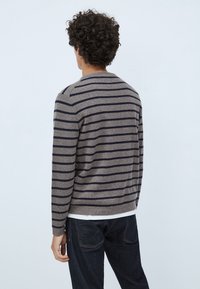 Maglione a righe grigio con strisce blu navy, realizzato in morbido materiale lavorato a maglia. Presenta un colletto rotondo e polsini a coste. Indossato con jeans scuri.