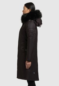 Pitkä musta toppatakki tekoturkiskuviollisella hupulla, sivutaskuilla ja vetoketjusomisteilla. Sileä pinta ja polven pituinen design.