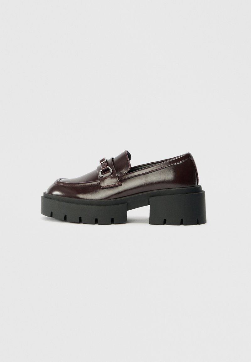 Mocassin en cuir marron foncé avec détail de boucle argentée et semelle plateforme noire épaisse et robuste avec talon.