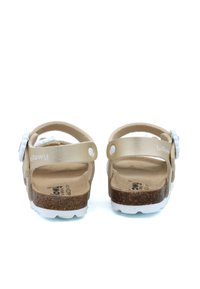 Sandales en cuir beige avec des accents blancs, semelle en liège, sangles réglables et ferrures décoratives en forme de fleur. Design plat et léger.