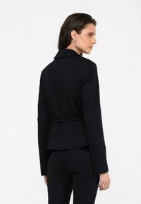 Blazer negro ajustado con diseño peplum, mangas largas y un cinturón a la altura de la cintura. Presenta un cuello con muesca y una textura de tela suave.
