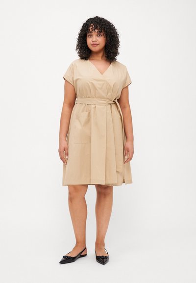 Beige wrap dress with short sleeves, v-neck, and tie waist. Features a simple design and falls above the knees. Paired with black pointed flats.