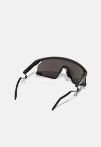 Ochelari de soare negri cu design în jurul feței, lentile întunecate, brațe subțiri și un cadru robust. Prezintă o formă geometrică minimalistă.