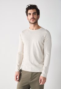 T-shirt crème à manches longues en tissu doux et texturé, avec un col rond et une coupe slim, associé à un pantalon vert olive.