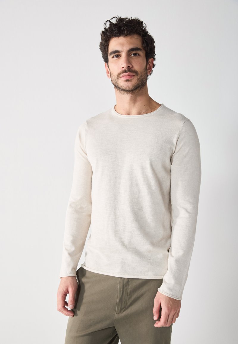 T-shirt crème à manches longues en tissu doux et texturé, avec un col rond et une coupe slim, associé à un pantalon vert olive.