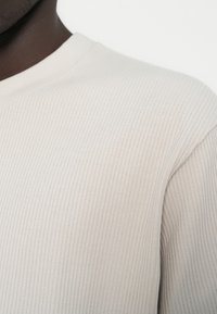 Ελαφρώς μπεζ μακρυμάνικη μπλούζα με ριγέ υφή, στρογγυλεμένο λαιμόκοψη και υφασμάτινη επιφάνεια με λεπτές κάθετες γραμμές και εφαρμοστή σχεδίαση.