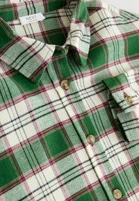 Grøn og creme plaid flannel skjorte med burgunder detaljer. Har en spids krave, to knapper og blød tekstur. Next mærkeetiket synlig.