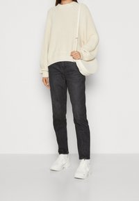 Krämfärgad stickad tröja med ruggad textur, kombinerad med mörka jeans och vita sneakers. Tillbehören inkluderar en vit axelväska.