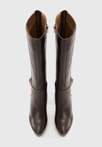 Ζευγάρι ψηλών, σκούρων καφέ δερμάτινων μπότες με πλευρικά φερμουάρ και αγκράφες, μυτερές μύτες και λεία υφή, φαντασμένες από πάνω.