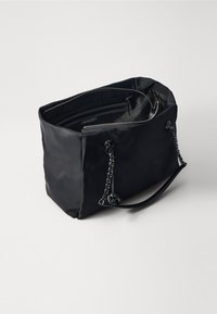 Borsa tote nera in nylon con accenti in catena, chiusura con zip e una sola tracolla. Gli interni presentano più scomparti.