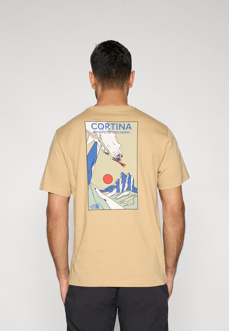 Μπεζ μπλουζάκι με πολύχρωμο γραφικό σχέδιο στην πλάτη, που απεικονίζει βουνά, έναν σκιέρ και τον ήλιο. Κοντά μανίκια, κανονική εφαρμογή.