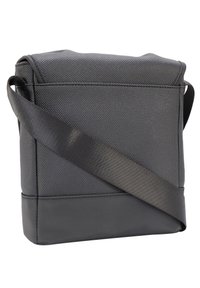 Borsa a tracolla nera con tessuto testurizzato, pannello inferiore liscio e una larga tracolla regolabile. Forma quadrata compatta, design minimalista.