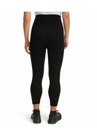 Leggings neri a vita alta con una texture liscia, lunghezza cropped e dettagli con cuciture minime, indossati con scarpe da ginnastica nere.