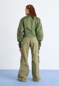 Olijfgroen bomberjack met een aansluitende taille, oversized opbollende mouwen, gecombineerd met loszittende olijfgroene cargobroek met zijzakken.