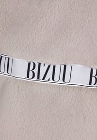 Faux futro w jasnoszarym kolorze o gładkiej fakturze, z wyraźną białą wstążką z czarnym logo "BIZUU".