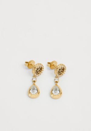 Boucles d'oreilles en or avec un dessus rond arborant un logo et entouré de strass transparents. Une pendeloque en cristal en forme de goutte d'eau pend en dessous.