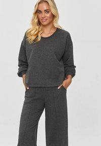Szary krótki sweatshirt z długimi rękawami i bocznymi kieszeniami, w połączeniu z szerokimi szarymi spodniami. Miękka tekstura i luźny krój.