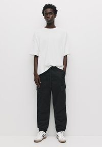 Witte oversized t-shirt gecombineerd met zwarte cargo pants met zakken. Sneakers met een witte basis en zwarte strepen maken de look compleet.