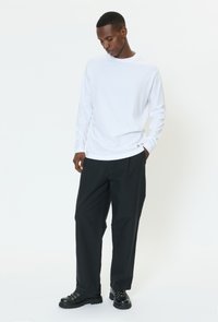 Vit skjorta med långa ärmar kombinerad med svarta byxor med vida ben och svarta snörstövlar, med enkel design och avslappnad passform.