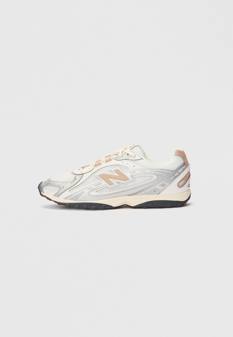 Sneaker da sport in grigio chiaro con accenti argentati, tomaia in rete, dettagli beige e suola in gomma nera. Presenta lacci e colletto imbottito.